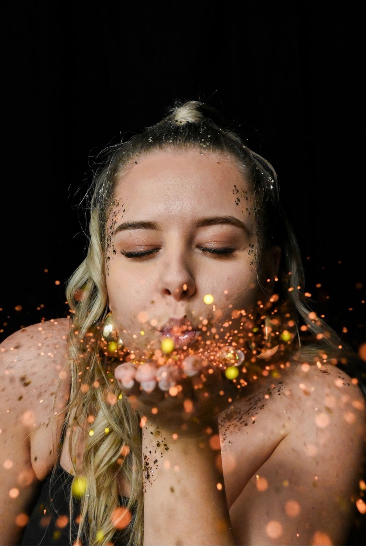 Justine souffle des paillettes dorées, sur fond noir