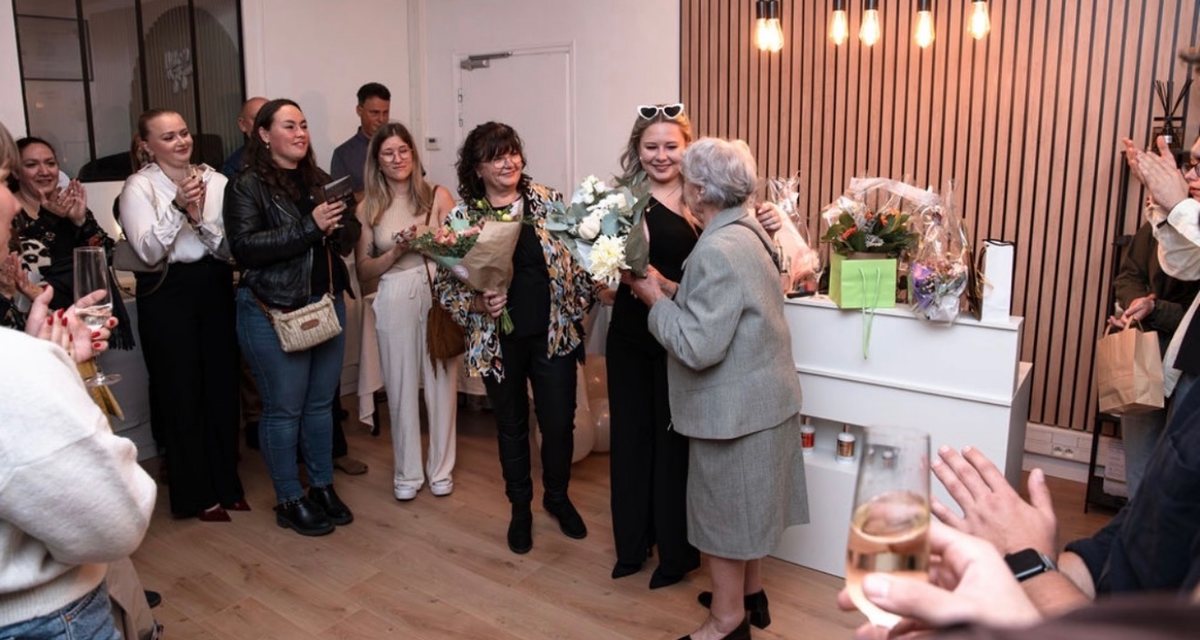 Justine entourée des invités, des bouquets de fleurs dans les mains, lors de l’inauguration
