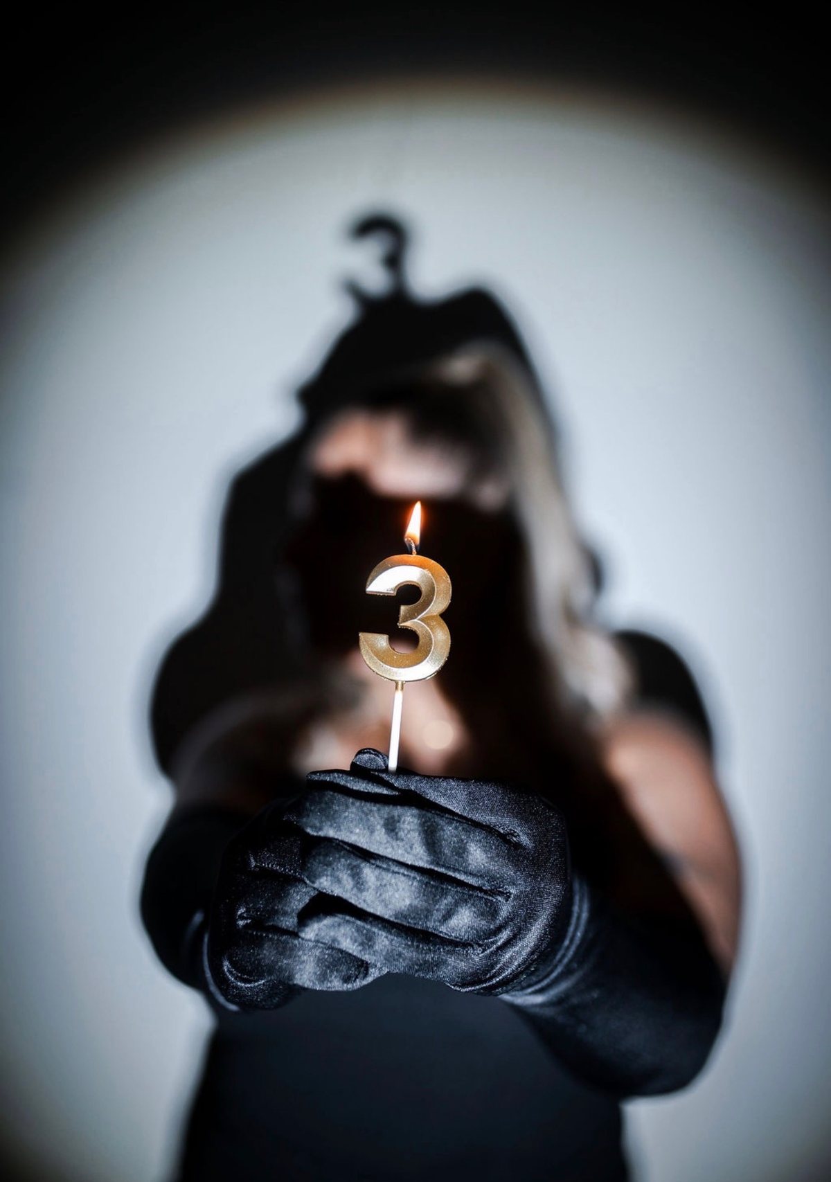 Une bougie chiffre 3 allumée, tenue par des mains gantées de noir